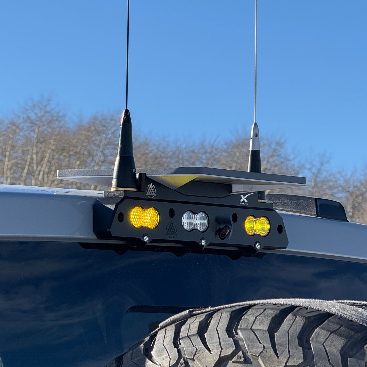 A close-up image of a black billet third brake light mounted on the top of a vehicle, featuring a rectangular housing with integrated LED lights and a brass NMO antenna mount.